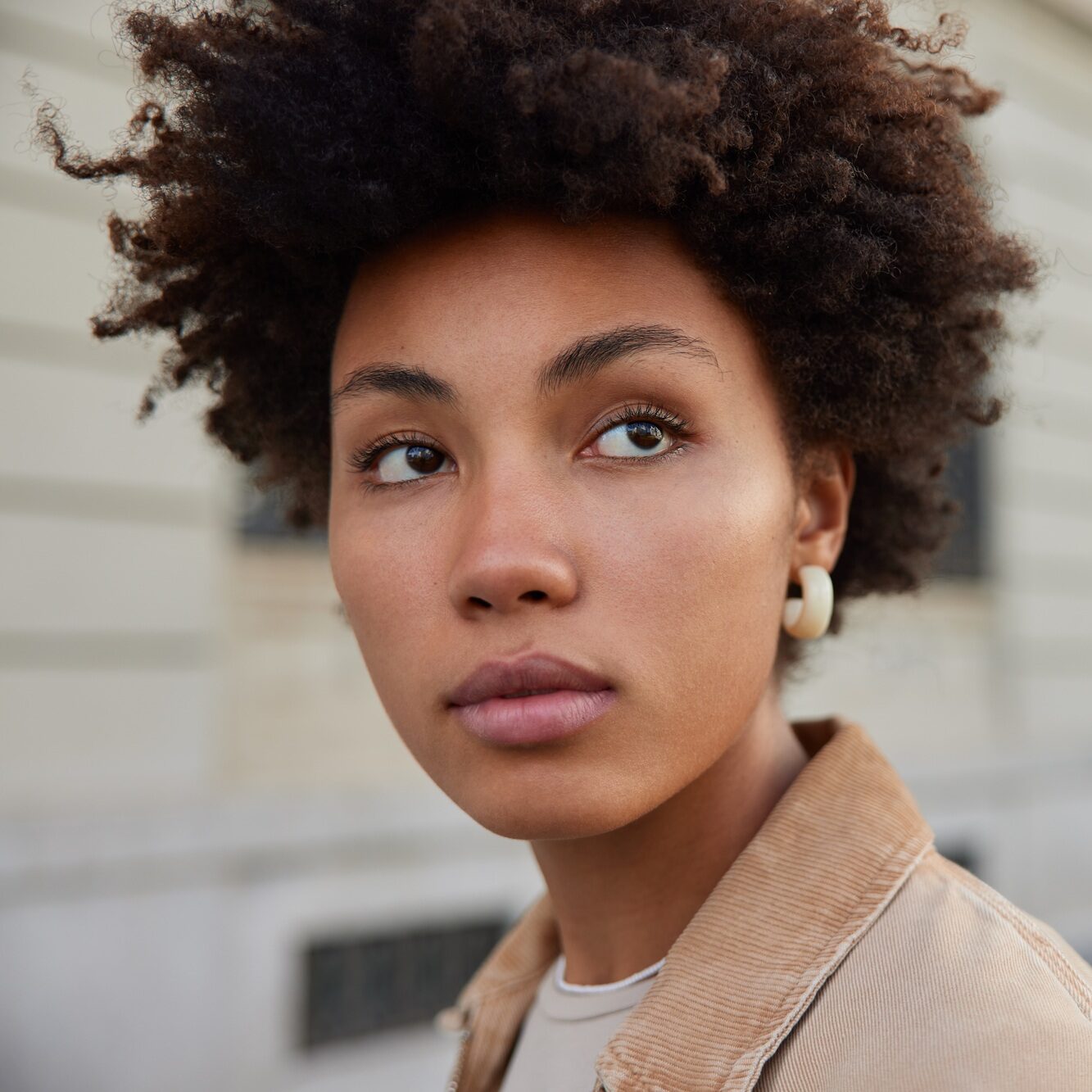 Headshot of good looking young woman with Afro hair looks attentively somewhere focused into distanc